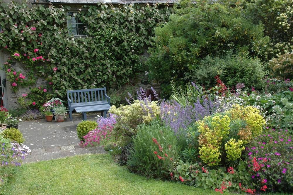 Staudenbeet im Garten neben kleiner Terrasse mit Bank